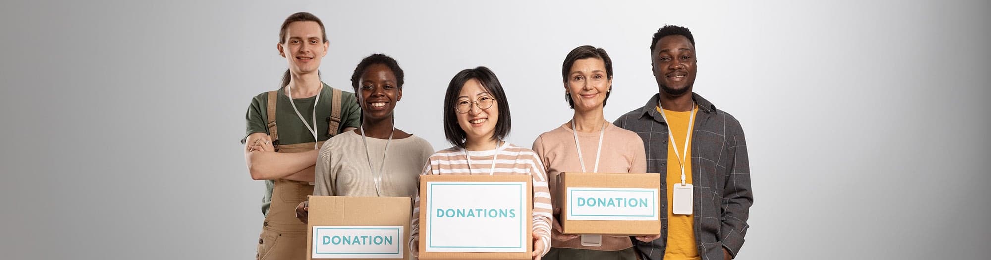 Five volunteers standing together holding cardboard boxes marked “Donations”