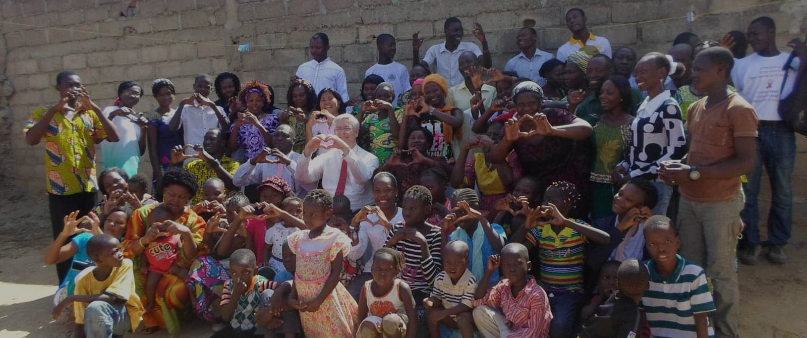 A large group of children and young people outdoors, smiling and making heart shapes with their hands