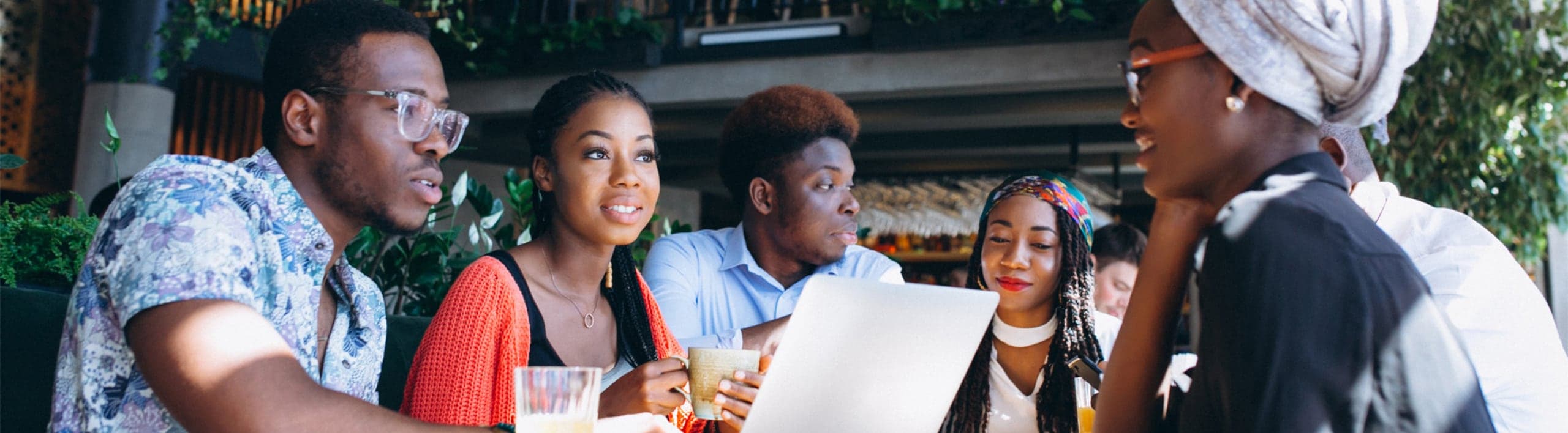 Five young people in conversation around a table, one holding a laptop
