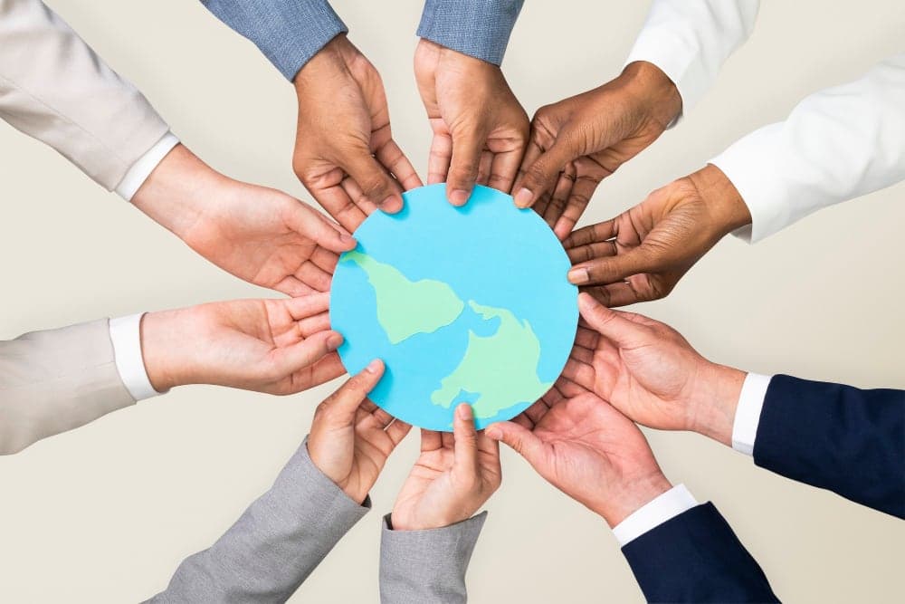Many hands from different people reaching in to hold a globe together