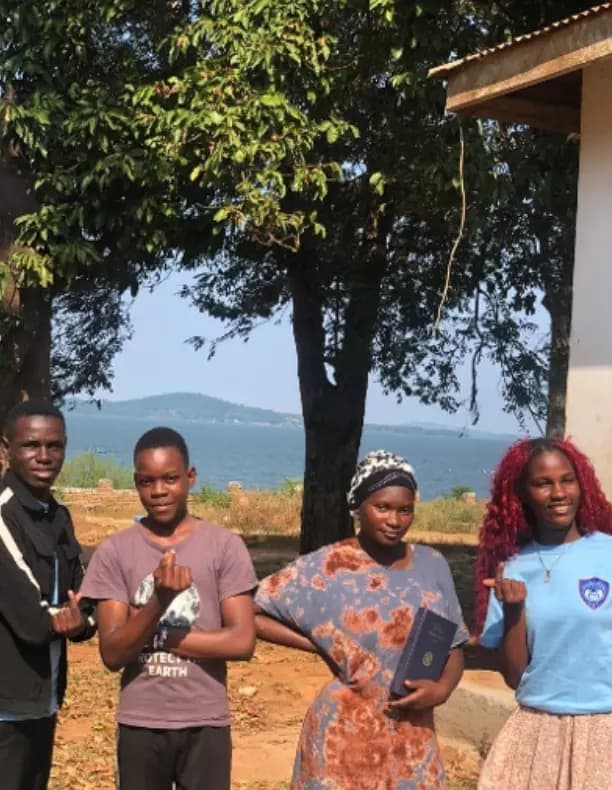 Four young people standing outdoors holding books.